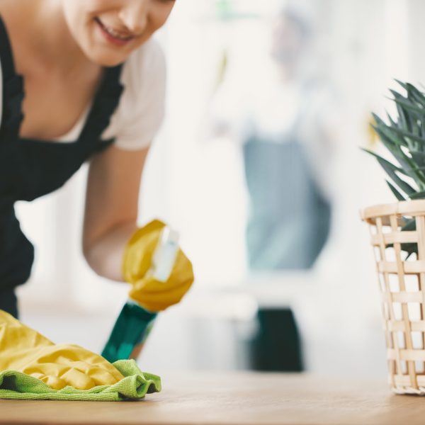 Close-up on smiling housewife with yellow gloves cleaning table with cloth